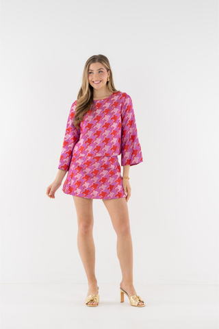 Emily McCarthy Ashley Ann Top in Houndstooth featuring a vibrant pink, red, and lavender pattern with flared sleeves and contrast trim.