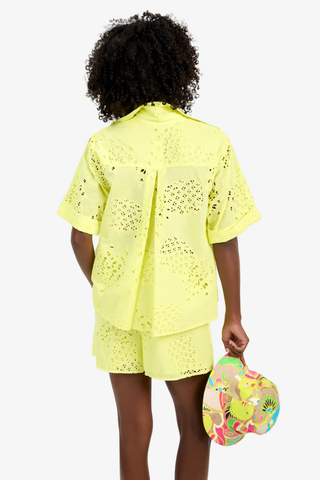 Model wearing the Trina Turk Triennale Top in Citrus featuring pineapple eyelet embroidery, short sleeves, and lace-up back detail with matching shorts