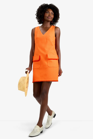Model wearing the Trina Turk Waveson Dress in Orange Oasis featuring textured jacquard fabric, fringe-trim patch pockets, sleeveless styling, and a V-neckline
