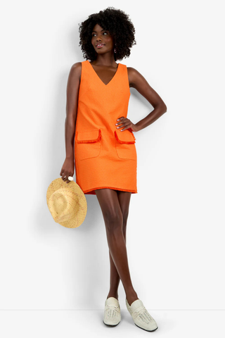 Model wearing the Trina Turk Waveson Dress in Orange Oasis featuring textured jacquard fabric, fringe-trim patch pockets, sleeveless styling, and a V-neckline